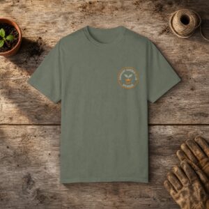 Dormant Garden Club Member gardening t-shirt in Moss, laid flat on a potting bench with gardening gloves and a trowel