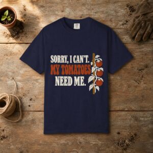 My Tomatoes Need Me gardening t-shirt in True Navy, laid flat on a potting bench with gardening gloves and a trowel