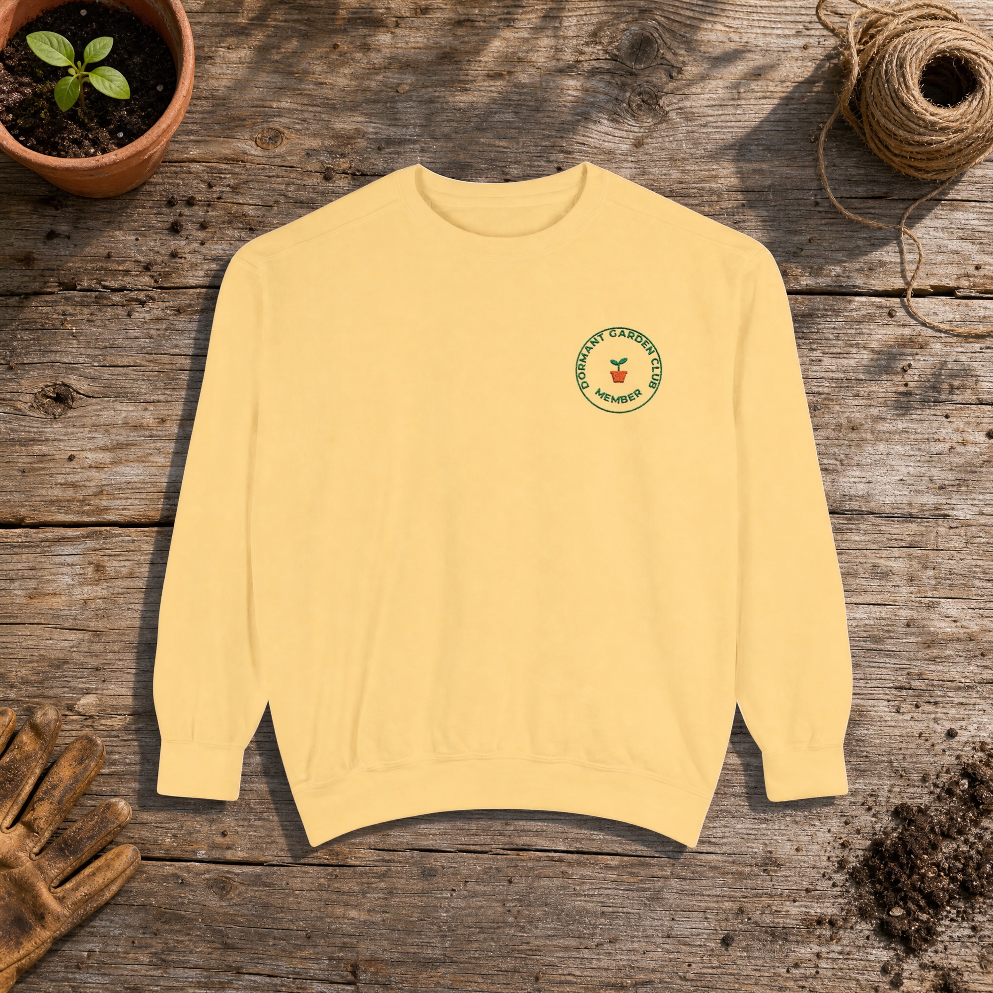 Dormant Garden Club Member Embroidered Sweatshirt in Butter, an embroidered crewneck sweatshirt on a potting bench