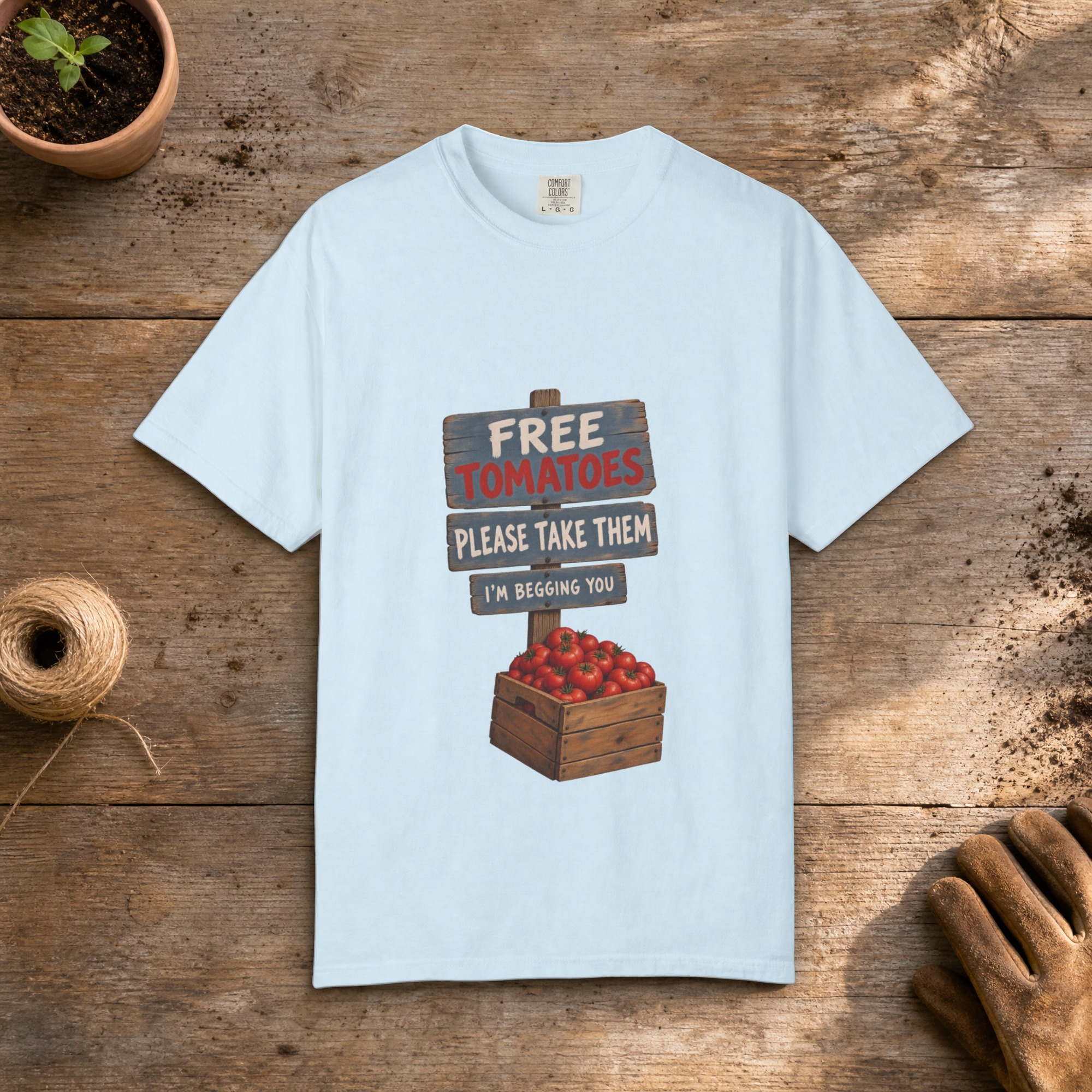 Free Tomatoes gardening t-shirt in Chambray, laid flat on a potting bench with gardening gloves and a trowel