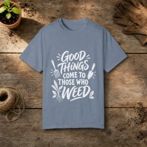 Good Things Come to Those Who Weed gardening t-shirt in Blue Jean, laid flat on a potting bench with gardening gloves and a trowel