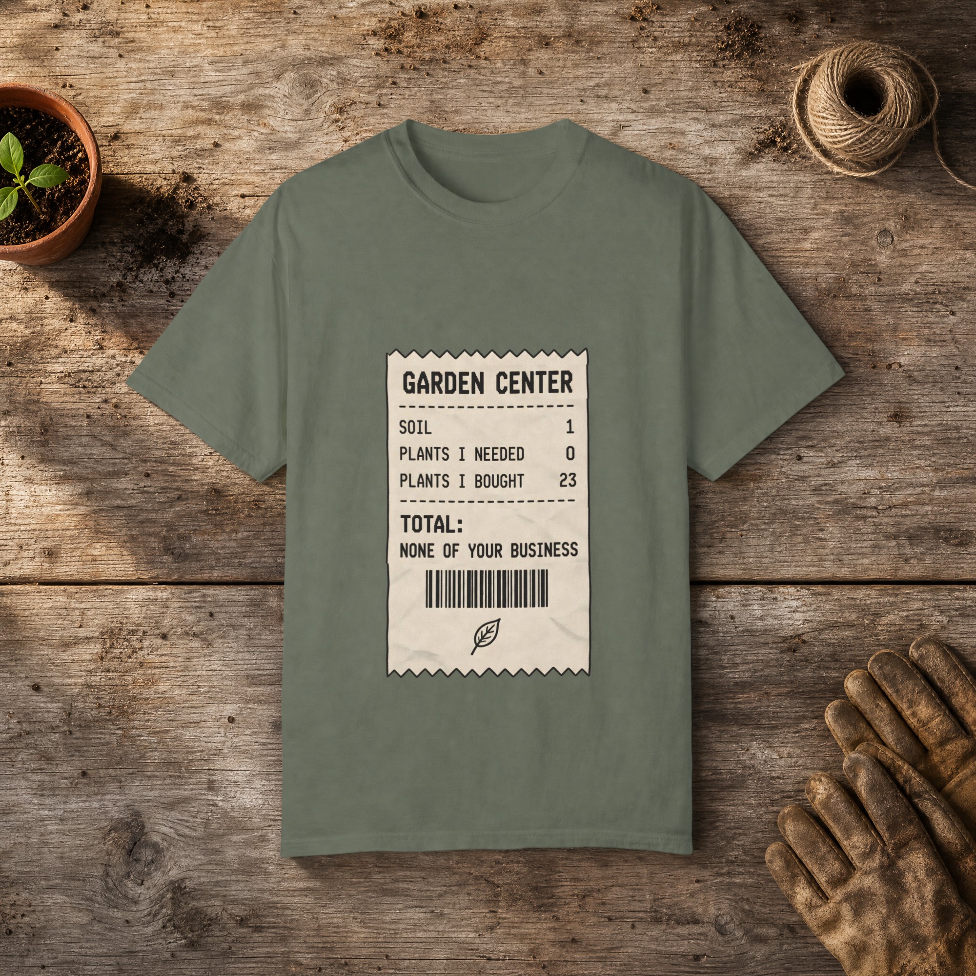 Garden Center Receipt gardening t-shirt in Moss, laid flat on a potting bench with gardening gloves and a trowel