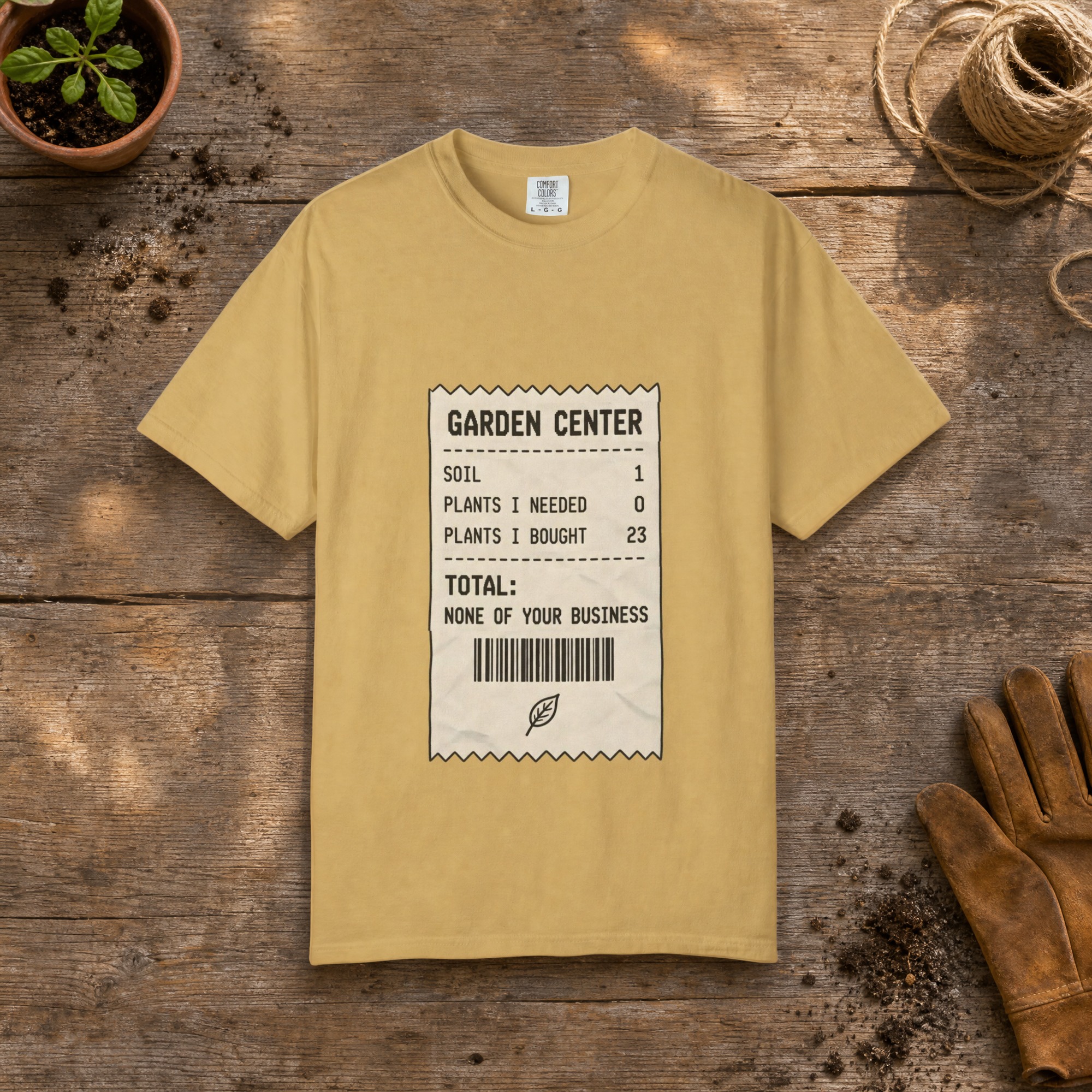 Garden Center Receipt gardening t-shirt in Mustard, laid flat on a potting bench with gardening gloves and a trowel