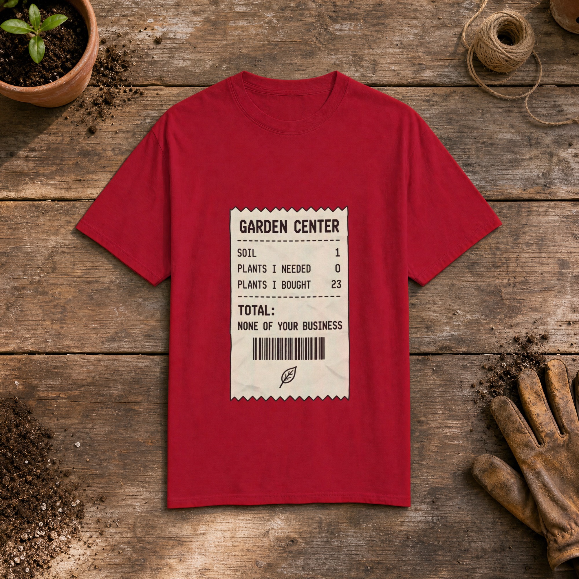 Garden Center Receipt gardening t-shirt in Red, laid flat on a potting bench with gardening gloves and a trowel