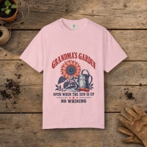Grandma's Garden gardening t-shirt in Blossom, laid flat on a potting bench with gardening gloves and a trowel