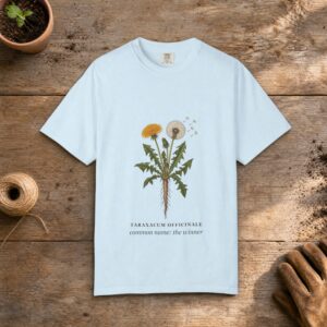 Dandelion Botanical gardening t-shirt in Chambray, laid flat on a potting bench with gardening gloves and a trowel
