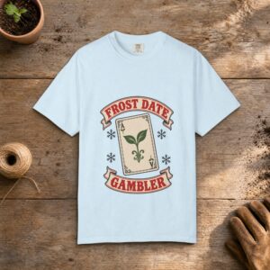 Frost Date Gambler gardening t-shirt in Chambray, laid flat on a potting bench with gardening gloves and a trowel