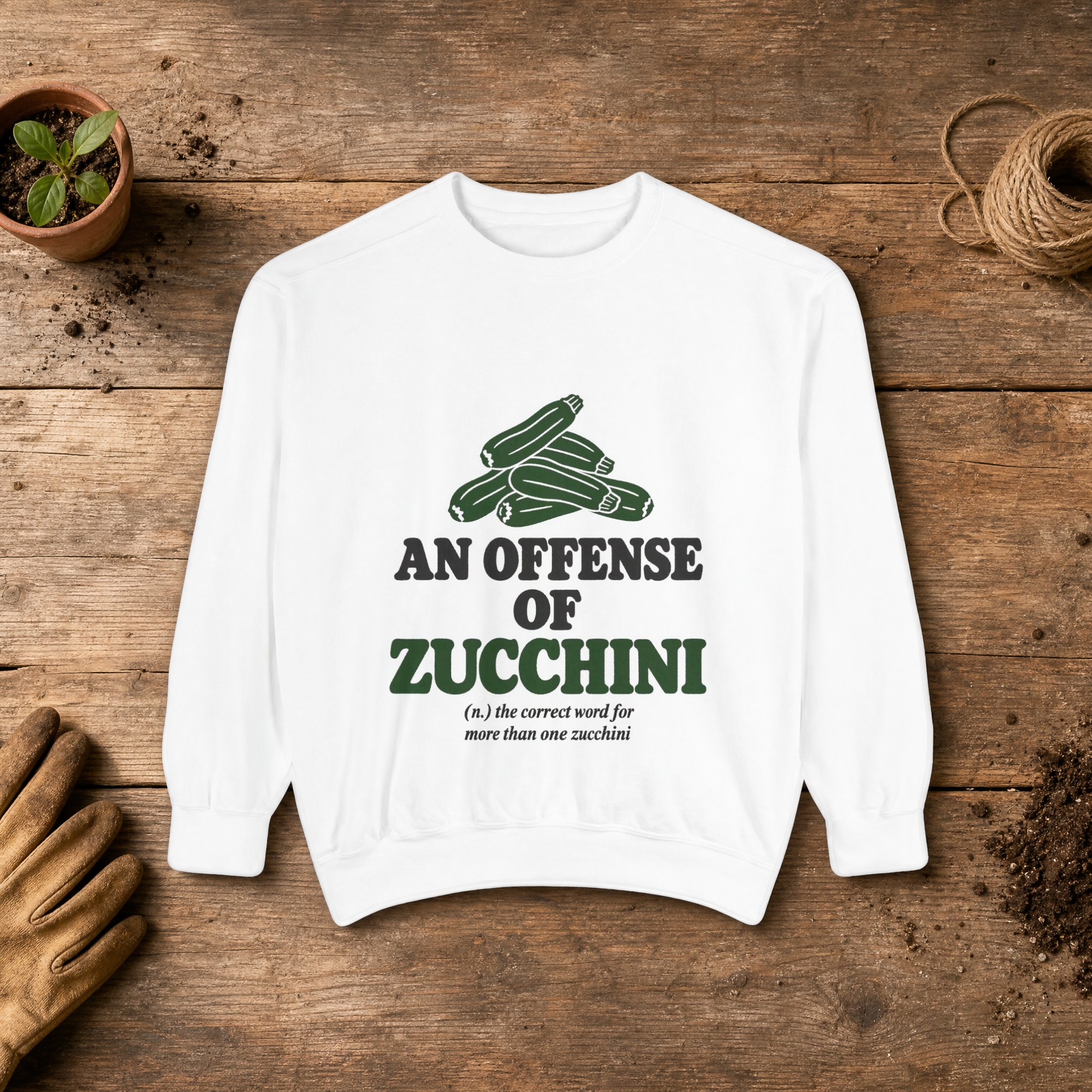 An Offense of Zucchini Sweatshirt in White, a crewneck sweatshirt on a potting bench