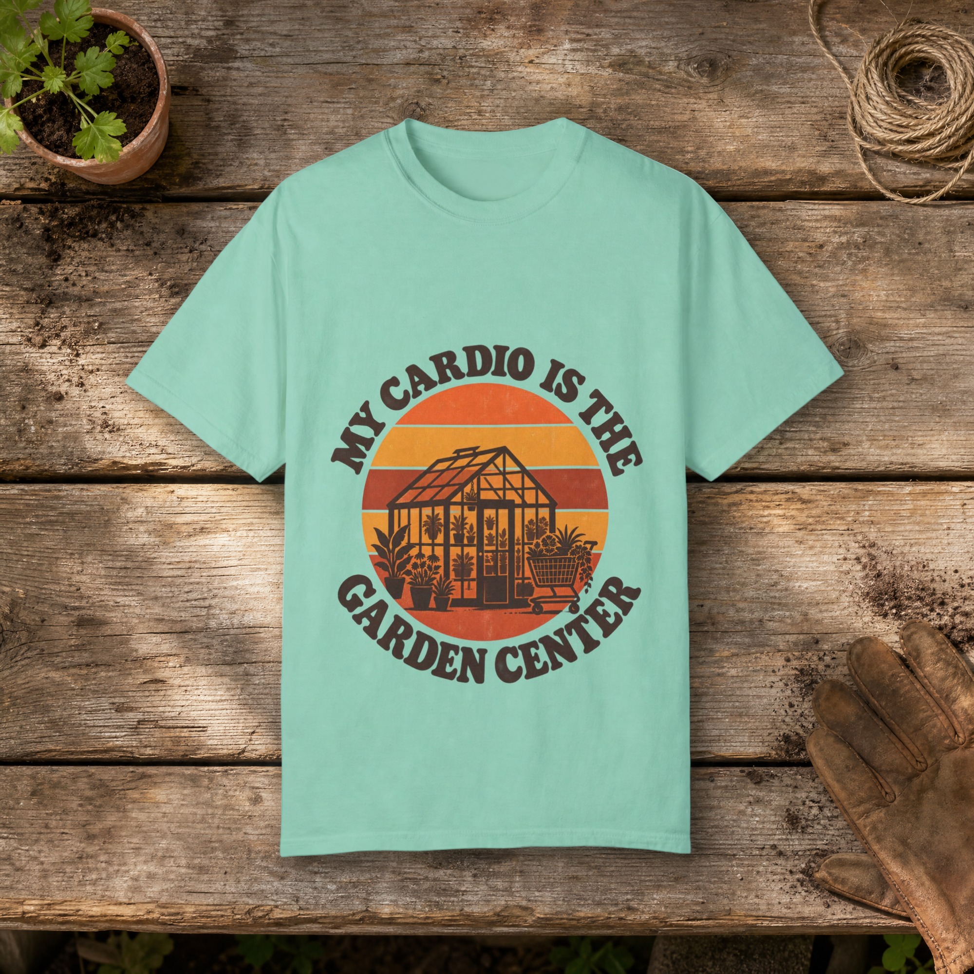 My Cardio Is the Garden Center gardening t-shirt in Island Reef, laid flat on a potting bench with gardening gloves and a trowel