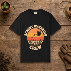 Sunset Watering Crew gardening t-shirt in Black, laid flat on a potting bench with gardening gloves and a trowel