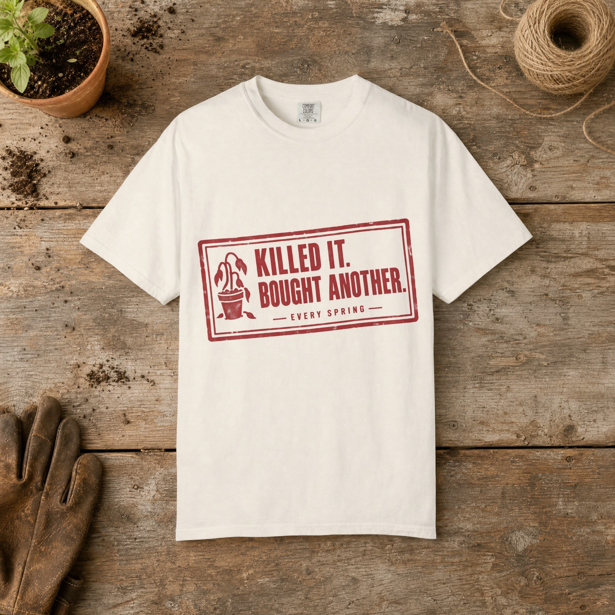 Killed It. Bought Another. gardening t-shirt in Ivory, laid flat on a potting bench with gardening gloves and a trowel