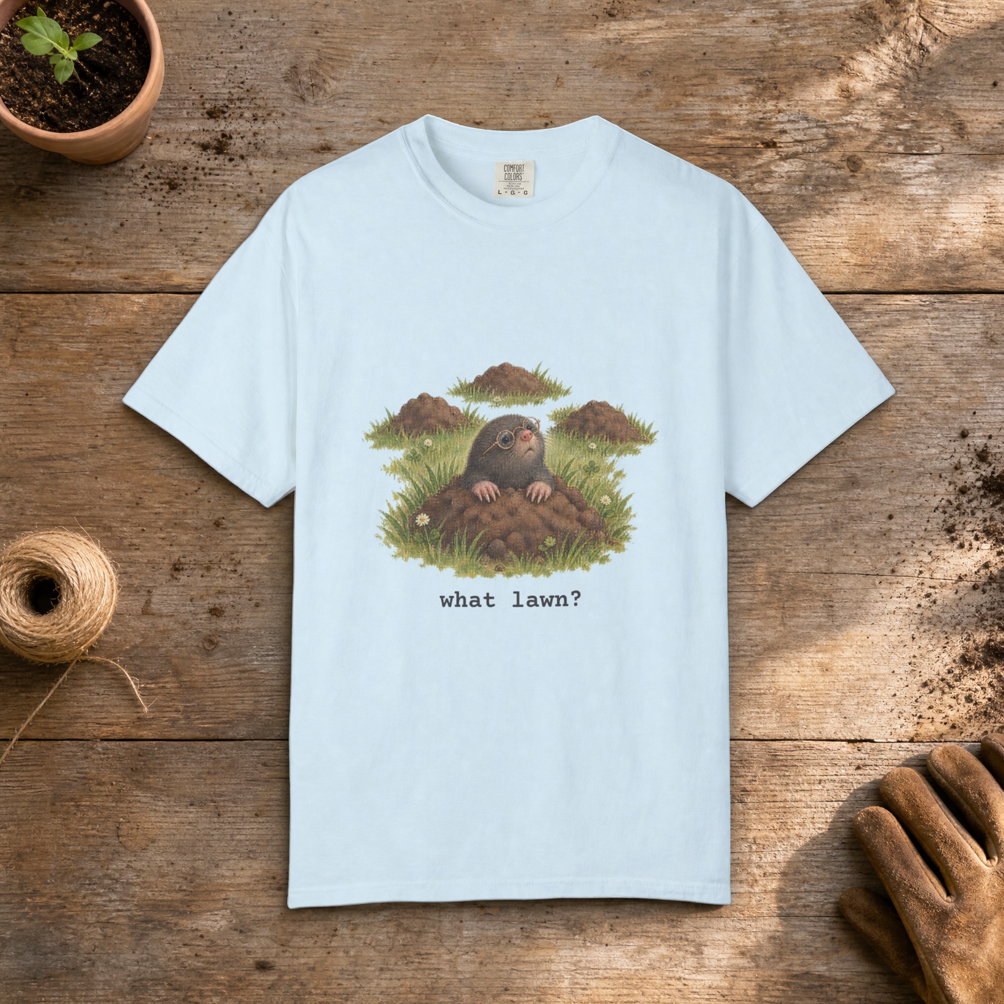 What Lawn gardening t-shirt in Chambray, laid flat on a potting bench with gardening gloves and a trowel
