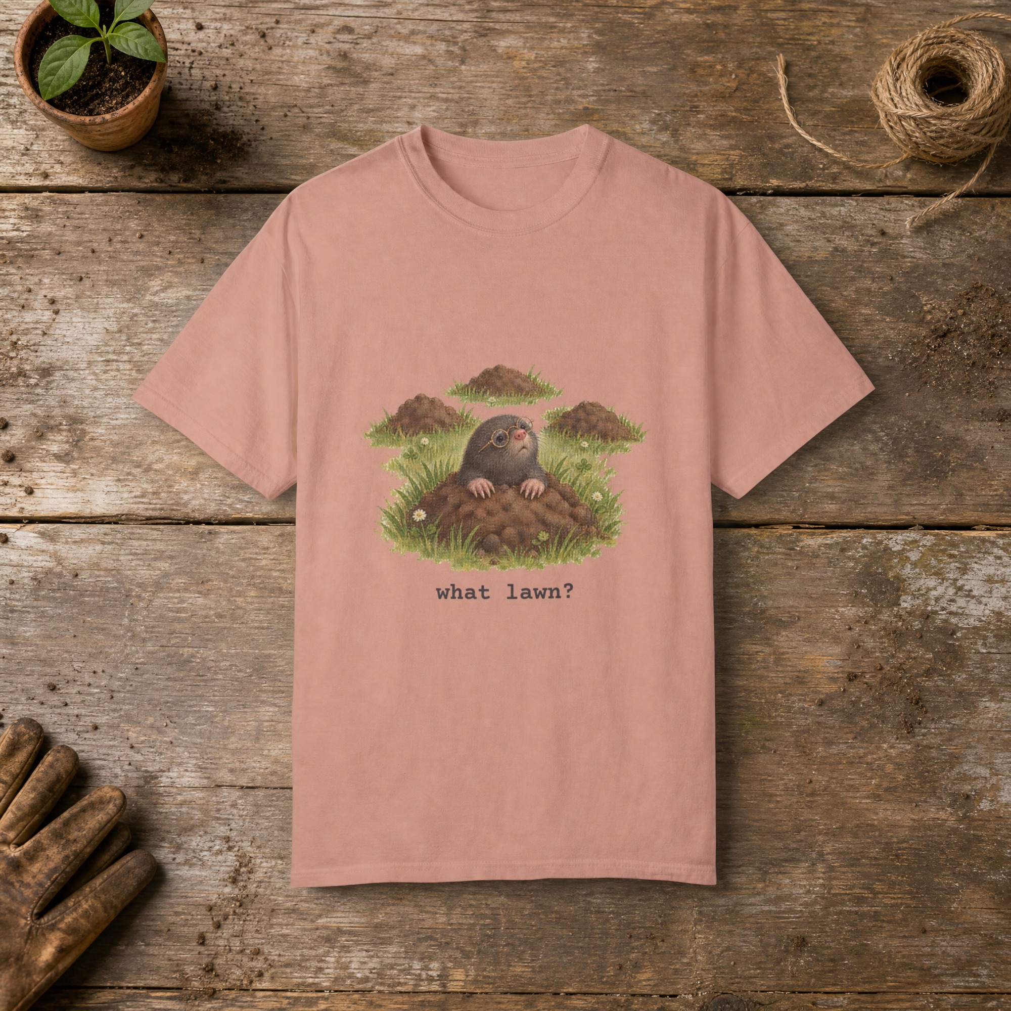 What Lawn gardening t-shirt in Peachy, laid flat on a potting bench with gardening gloves and a trowel