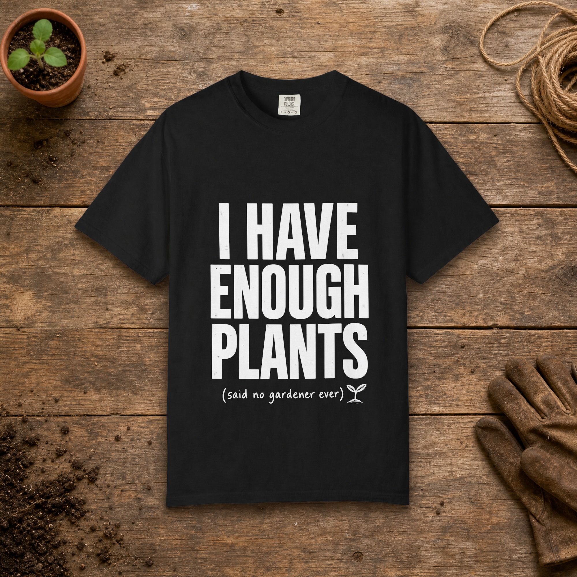I Have Enough Plants gardening t-shirt in Black, laid flat on a potting bench with gardening gloves and a trowel