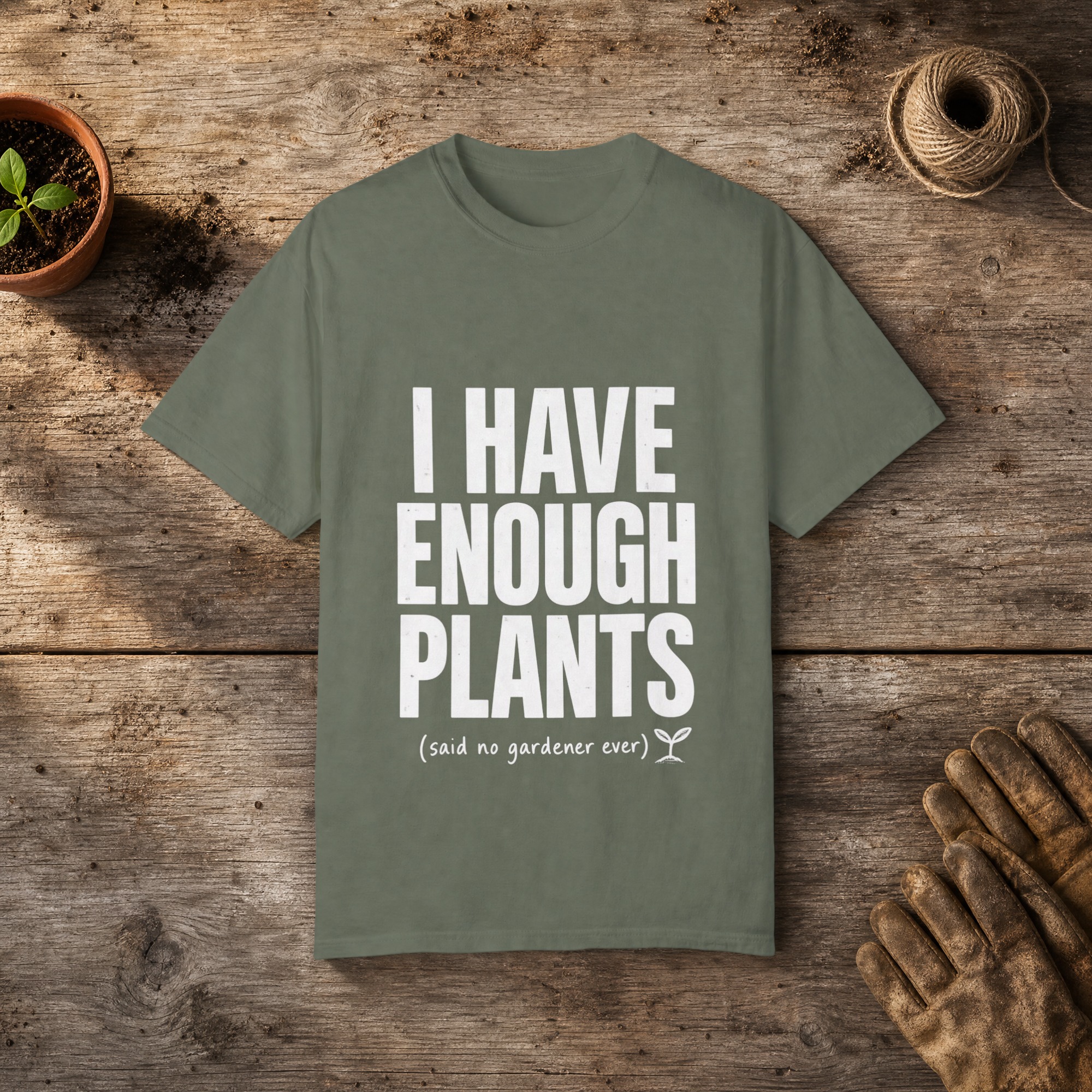 I Have Enough Plants gardening t-shirt in Moss, laid flat on a potting bench with gardening gloves and a trowel