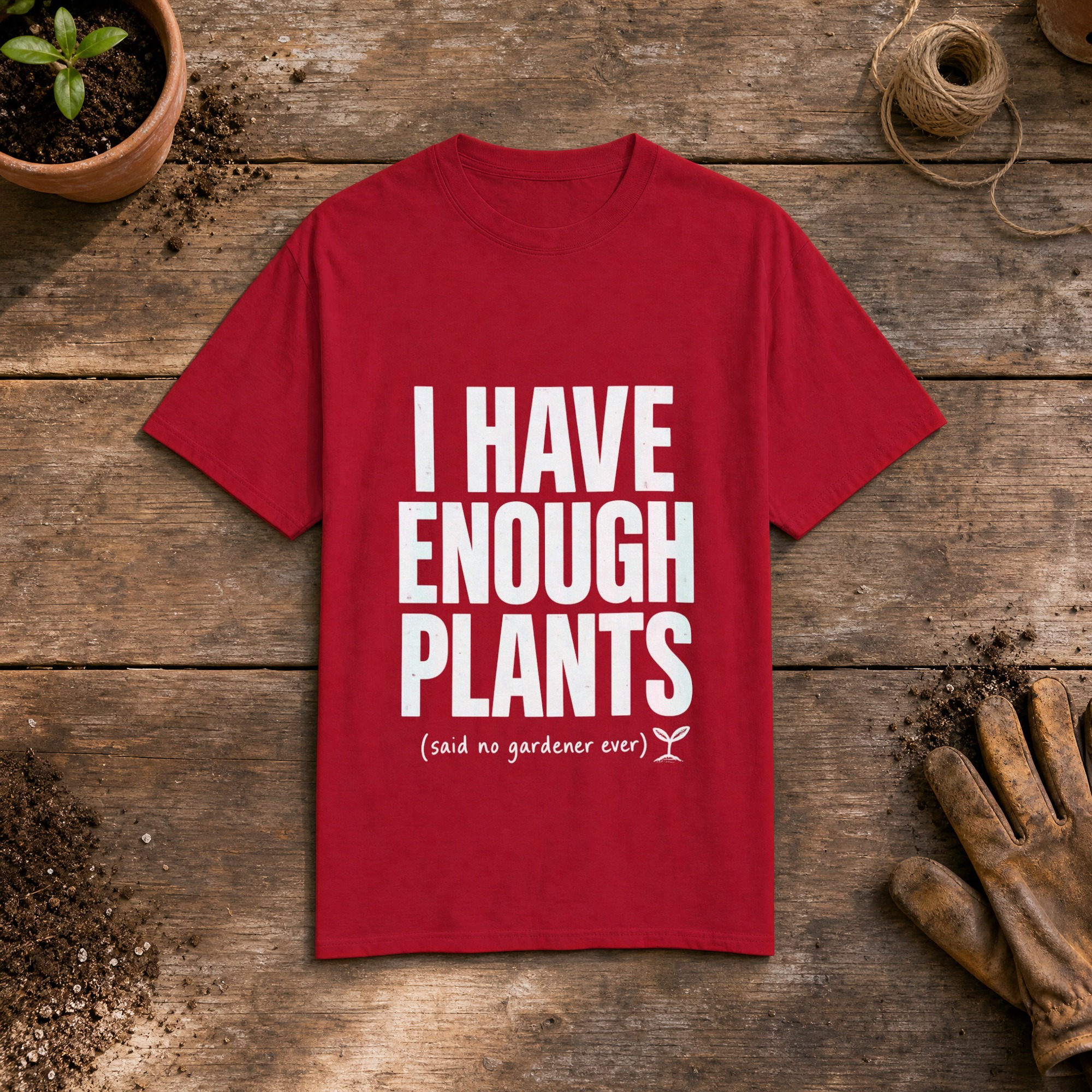 I Have Enough Plants gardening t-shirt in Red, laid flat on a potting bench with gardening gloves and a trowel