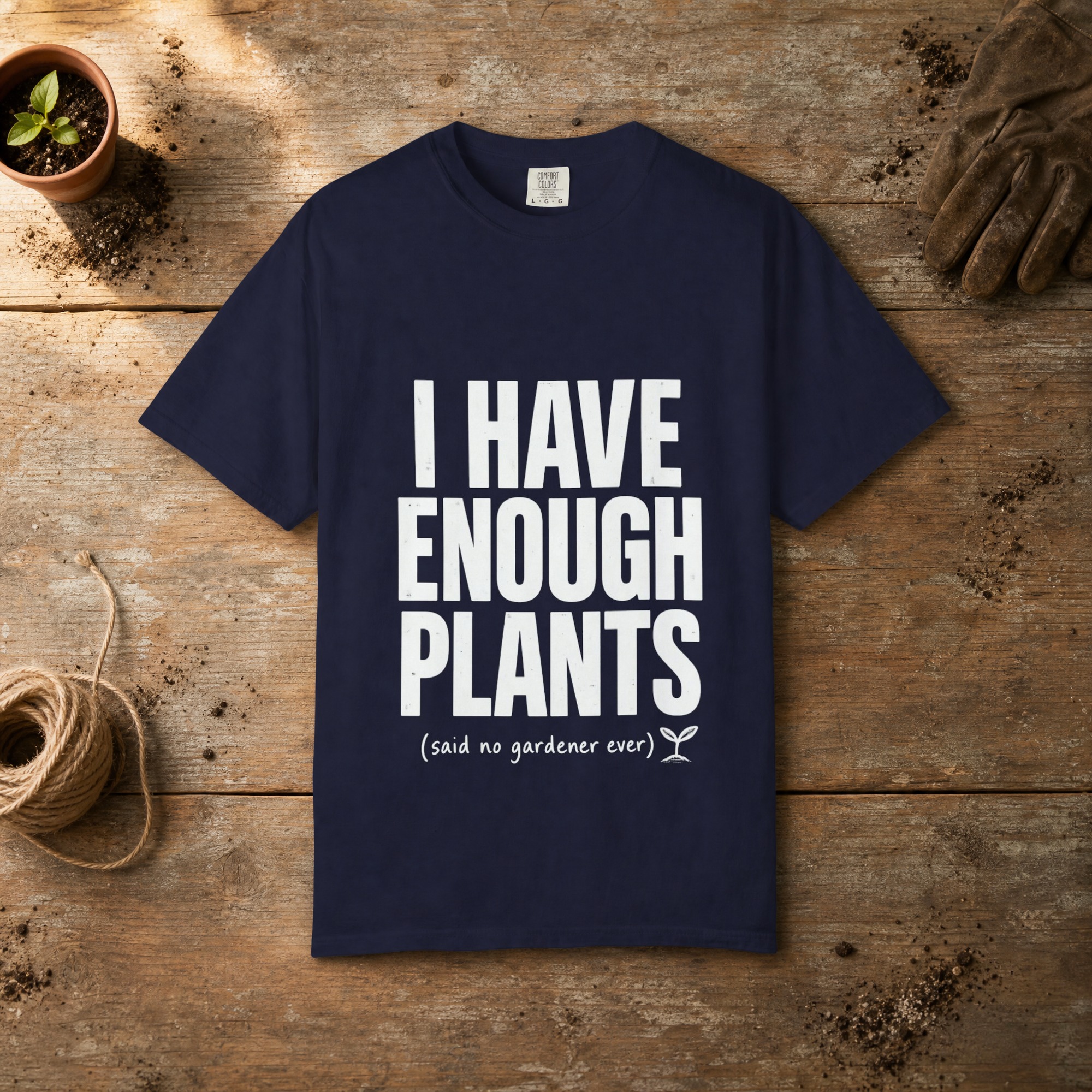 I Have Enough Plants gardening t-shirt in True Navy, laid flat on a potting bench with gardening gloves and a trowel