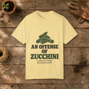 An Offense of Zucchini gardening t-shirt in Butter, laid flat on a potting bench with gardening gloves and a trowel