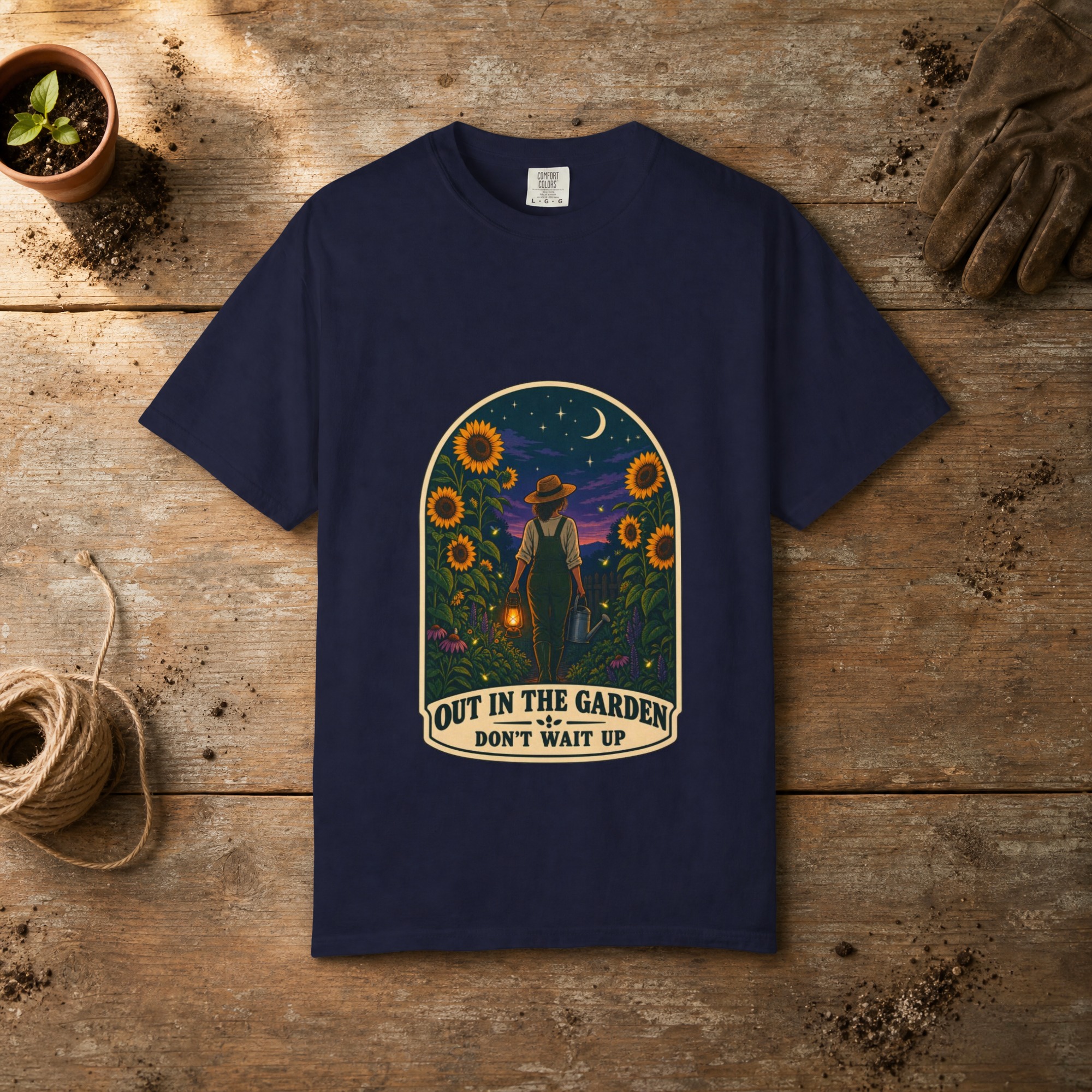 Out in the Garden gardening t-shirt in True Navy, laid flat on a potting bench with gardening gloves and a trowel