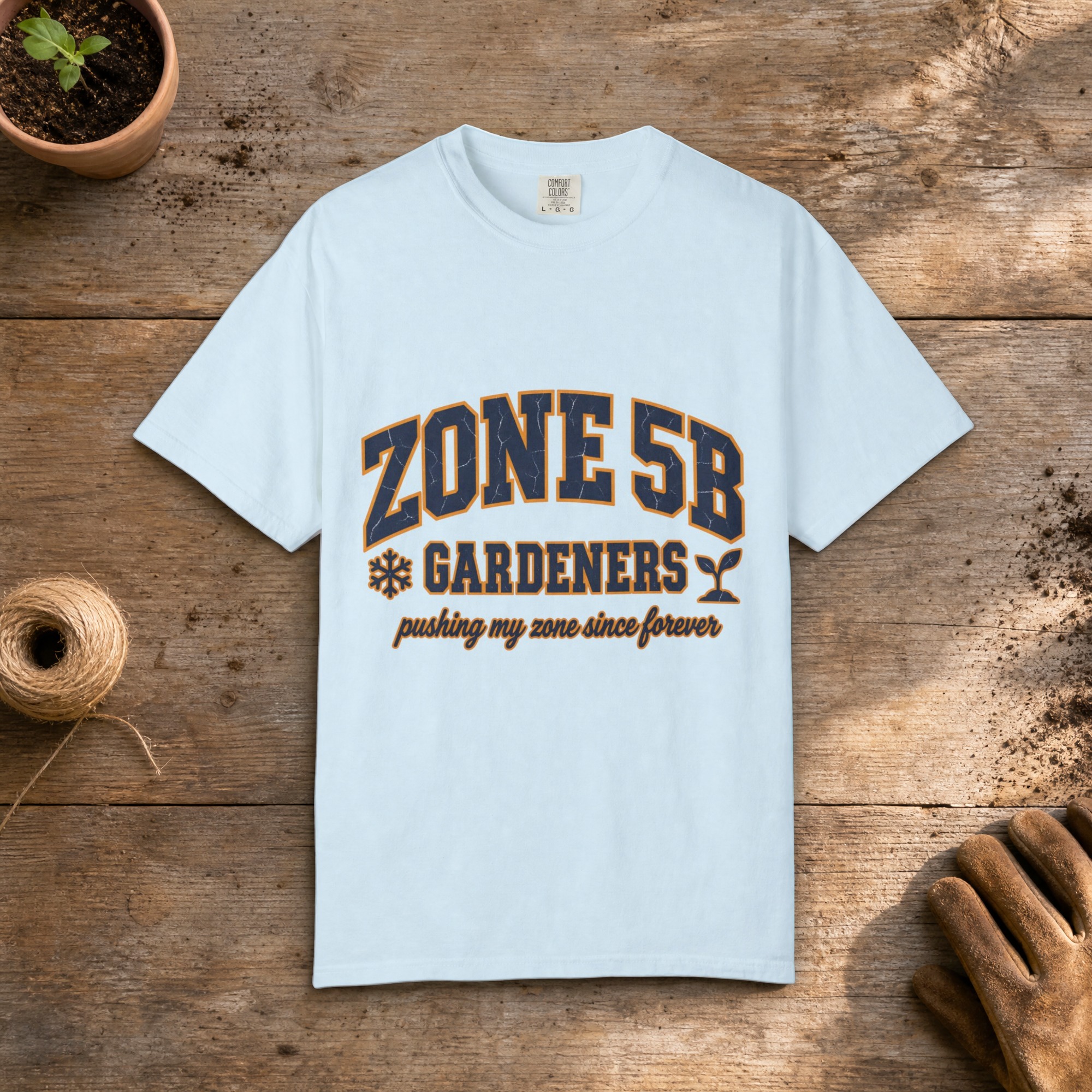 Zone 5B Gardeners gardening t-shirt in Chambray, laid flat on a potting bench with gardening gloves and a trowel