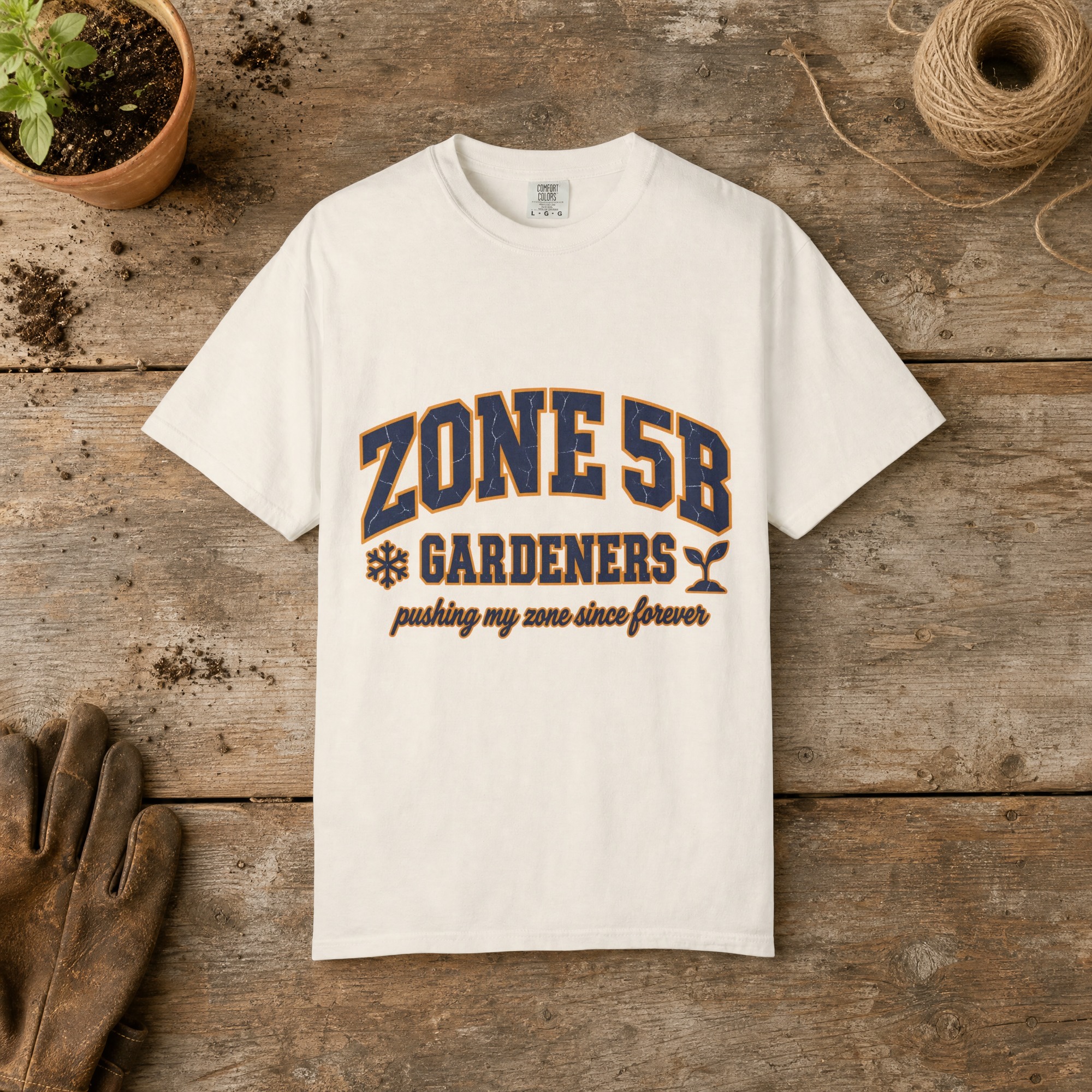 Zone 5B Gardeners gardening t-shirt in Ivory, laid flat on a potting bench with gardening gloves and a trowel