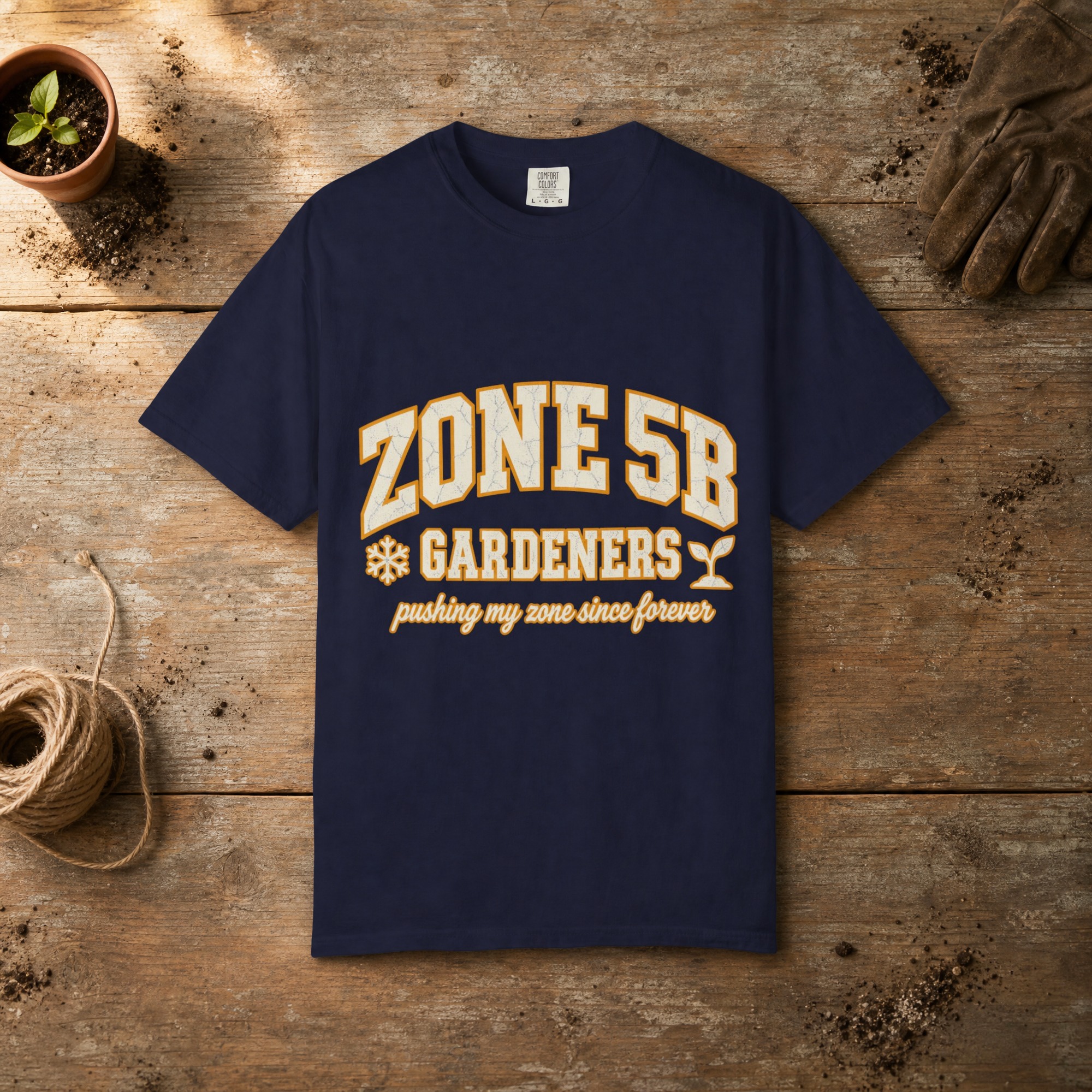 Zone 5B Gardeners gardening t-shirt in True Navy, laid flat on a potting bench with gardening gloves and a trowel