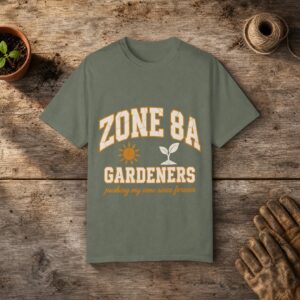 Zone 8A Gardeners gardening t-shirt in Moss, laid flat on a potting bench with gardening gloves and a trowel